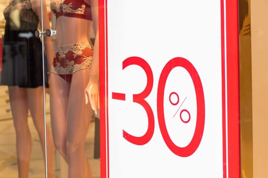 Discount percentage sign display in fashion department store during sale season period.