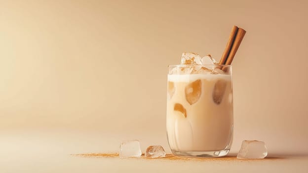 A refreshing iced drink, filled with ice cubes and topped with cinnamon sticks, rests on a smooth beige surface. The drink exudes a creamy texture, inviting to enjoy.