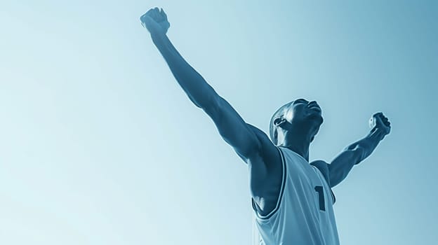 A young male athlete triumphantly raises his arms in celebration after winning a basketball game. The clear blue sky provides a vibrant backdrop, highlighting his excitement and the energy of the moment.