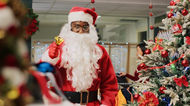 Worker dressed as Santa Claus entertaining shoppers in xmas adorn fashion store during winter holiday season. Retail assistant sharing festive spirit with customers visiting clothing shop