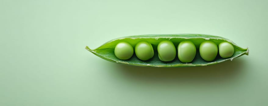 Close-up of fresh green peas in a pod against pastel green background. Nature and organic food concept.