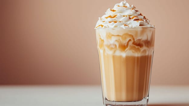 A tall glass filled with creamy coffee is topped with generous whipped cream and a caramel drizzle. The minimalist setting highlights the drink's inviting appearance and creamy texture.