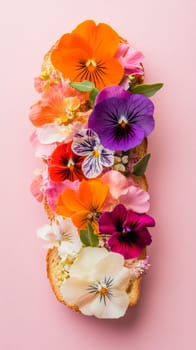 Open-faced sandwich with colorful edible flowers on pink background. Gourmet floral cuisine concept.