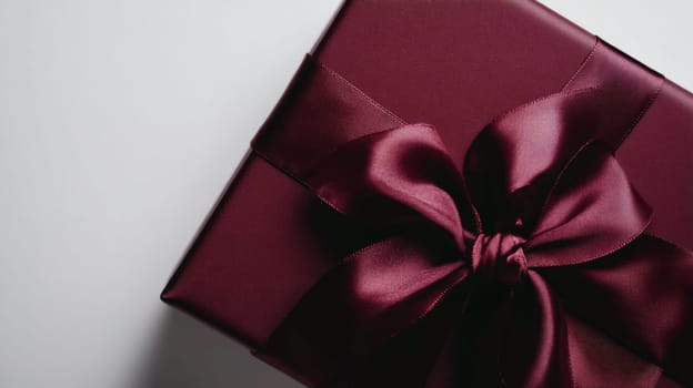 Burgundy gift box with satin ribbon bow, elegant celebration. Luxury gift and festive concept.