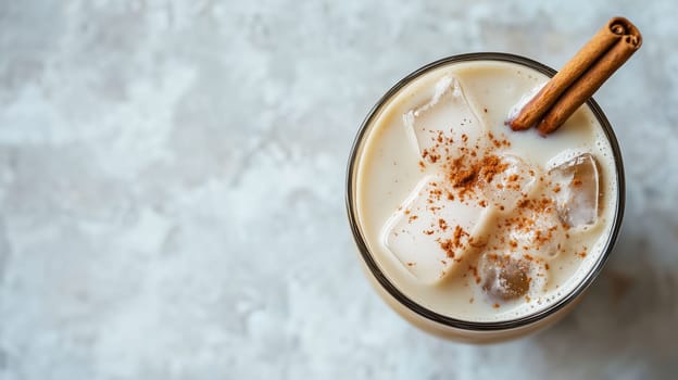 A refreshing iced drink features creamy milk, ice cubes, and a sprinkle of cinnamon on top, adding warmth to the cool beverage. Perfect for a warm afternoon treat.