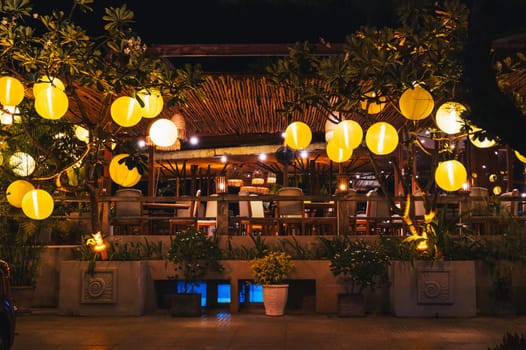 Yellow glowing Chinese lanterns decorate the exterior of a cafe in Vietnam in Asia