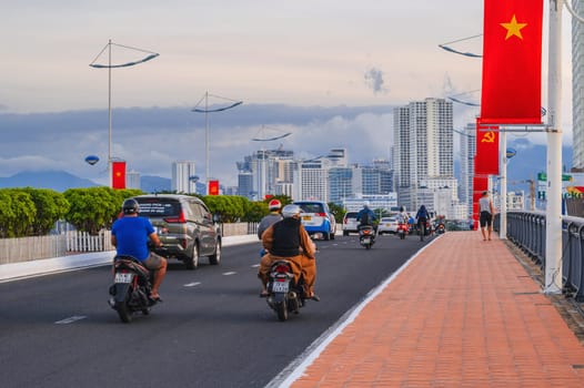 Motorbike transport traffic on the road on a bridge with Vietnam flags in a city in Asia in summer day. Nha Trang, Vietnam - August 22, 2024