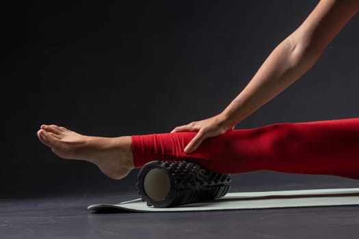 physiotherapy massage, woman with yoga roller on floor for leg tension on dark background, self massage with roller