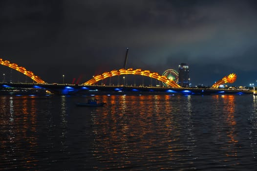 A famous landmark is the Dragon Bridge or Cau Rong over the Han River in Da Nang in Vietnam at night with a golden illumination