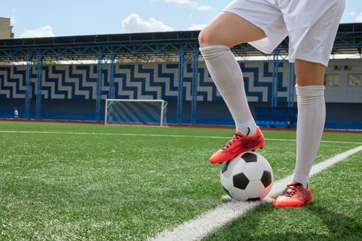 girl Football player in white shorts and red boots standing with soccer ball on green artificial turf field. women football concept