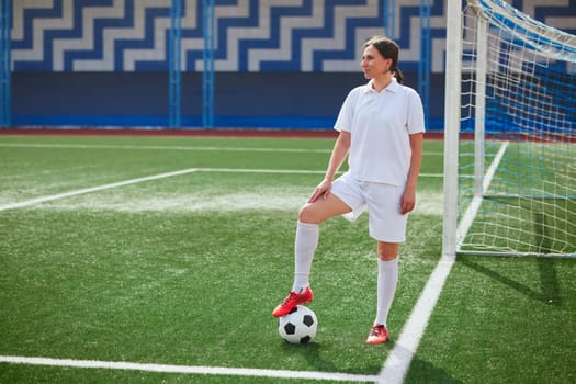 girl Football player in white shorts and red boots standing with soccer ball on green artificial turf field. women football concept