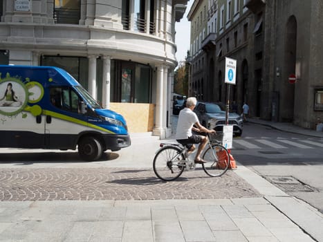 Cremona, Italy August 31st 2024 A senior man is riding a bicycle on a cobblestone street in an urban environment, passing by a delivery van