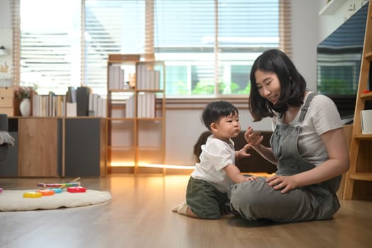 Happy young mother playing cute little boy on floor at home. Childhood and nurturing care concept.