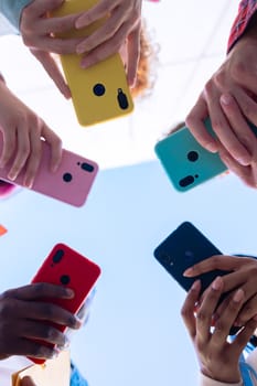 Low-angle shot of a group of diverse hands holding brightly colored smartphones, forming a circle. The photo showcases modern communication and social media interaction in a vibrant, connected setting