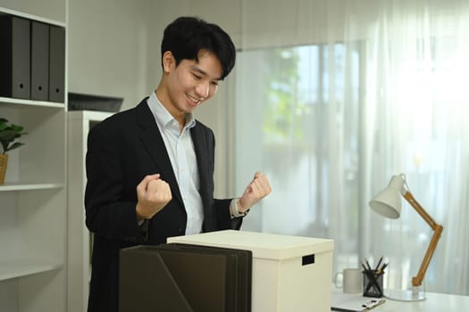 Happy asian male office worker with box of his belongings moving into a new office.