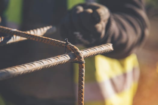 A worker uses steel tying wire to fasten steel rods to reinforcement bars close-up. Reinforced concrete structures - making a steel reinforcing cage for concrete beam