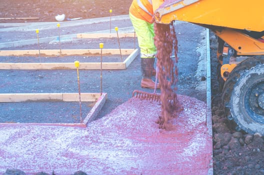 Builders pouring and levelling wet ready-mix concrete into formwork   during new footpath construction