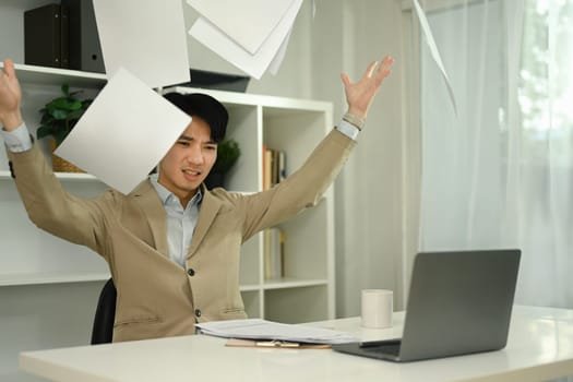 Overworked angry businessman throwing papers in the air with emotional stress in his office.