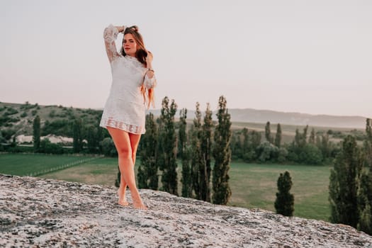 Romantic beautiful bride in white dress posing with sea and mountains in background. Stylish bride standing back on beautiful landscape of sea and mountains on sunset