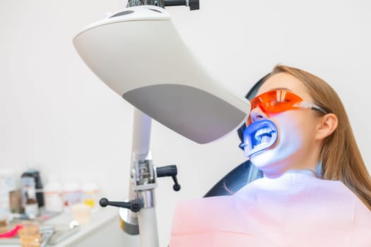 A female patient receives teeth whitening treatment, including the use of a UV lamp for bleaching at dentist clinic