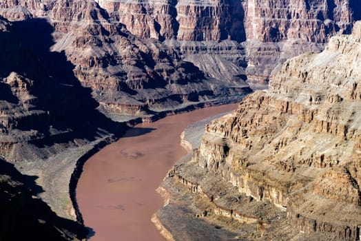Witness the mighty Colorado River as it winds through the base of Grand Canyon West, captured at an elevation of 1,160 ft (350 m) in this high-resolution photograph. The image provides a mesmerizing perspective on the river role in carving this iconic landscape over millennia. The water emerald hue contrasts beautifully with the towering red-rock formations, creating a scene of breathtaking grandeur. Perfect for adding a sense of depth and history to your home, office, or digital project
