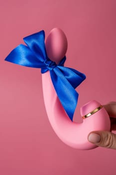 Woman holding curved dildo with blue ribbon on pink background