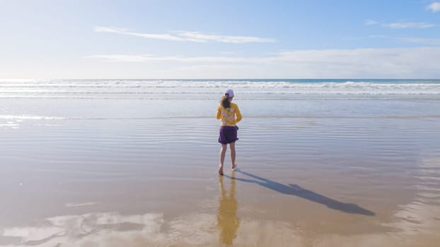 Little girl, braving the cold, joyfully runs in her swimsuit across the beach during winter.