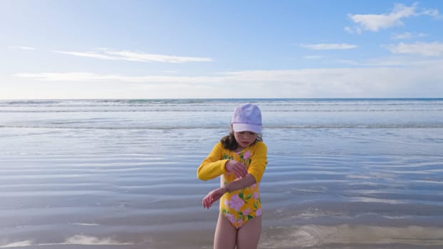 Little girl, braving the cold, joyfully runs in her swimsuit across the beach during winter.