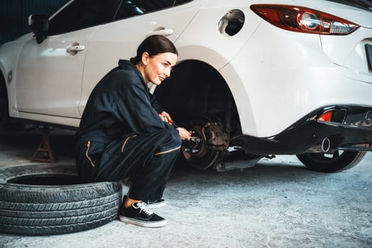 Hardworking female mechanic changing car wheel in auto repair workshop. Automotive service worker changing leaking rubber tire in concept of professional car care and maintenance. Oxus