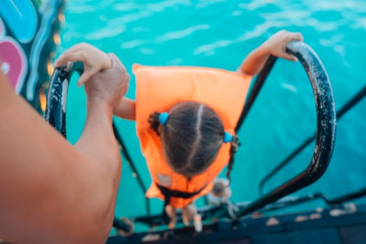 A young child, wearing a bright orange life vest, confidently climbs a tall ladder, excited for their water adventure
