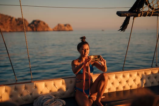 A woman happily enjoys her time on a boat, taking photographs of the beautiful, serene sunset over the sea
