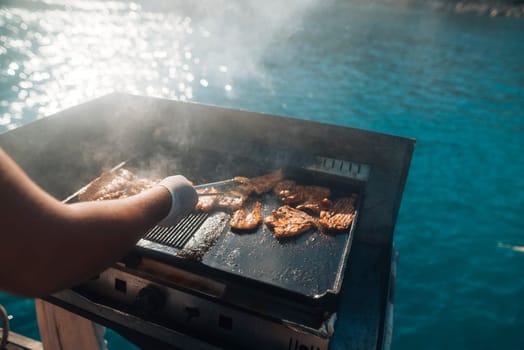 A skilled chef expertly grills a variety of fresh seafood on a portable grill beside stunning blue waters