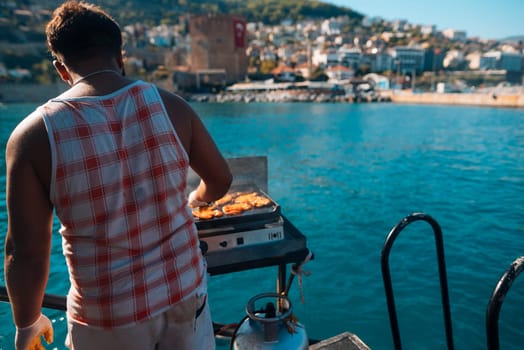 A man is grilling delicious seafood near the water, enjoying a stunning coastal view and delightful sunny weather