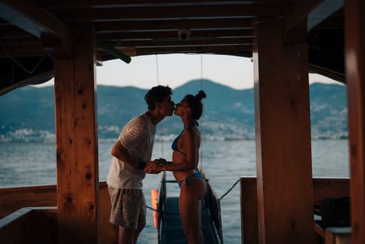 A couple shares a kiss on a boat at sunset, with peaceful waters and majestic mountains around them