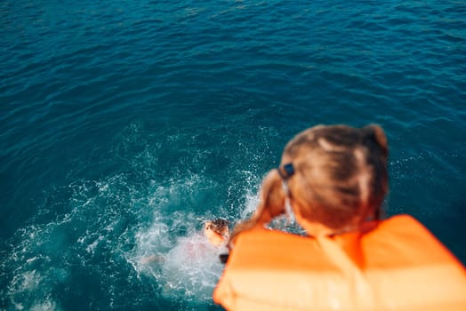 A child in a bright life jacket leaps joyfully into sparkling blue waters, embracing a thrilling summer adventure
