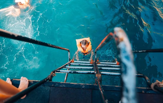 A swimmer climbs a sturdy ladder from a boat into clear turquoise waters, enjoying the summer vibes