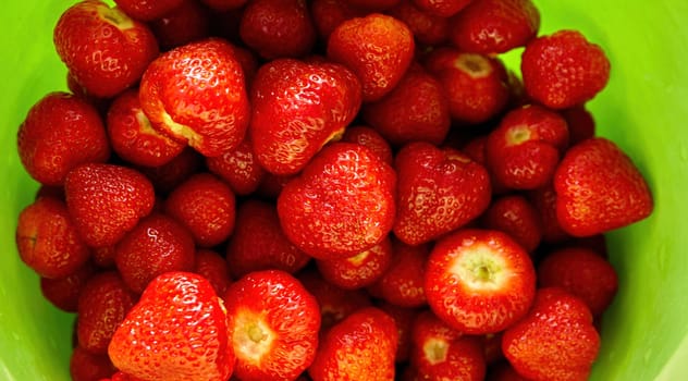 Sun-kissed strawberries, freshly picked and arranged beautifully, sit in a vibrant green bowl, radiating summer's warmth