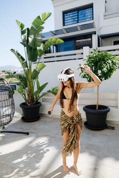 A woman immersed in virtual reality, joyfully dancing outdoors in a vibrant tropical setting with lush plants