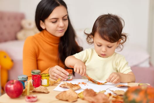 happy little child girl and her mother drawing for the autumn holiday. Autumn craft
