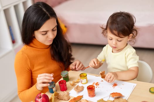 happy little child girl and her mother drawing for the autumn holiday. Happy family making autumn decorations together