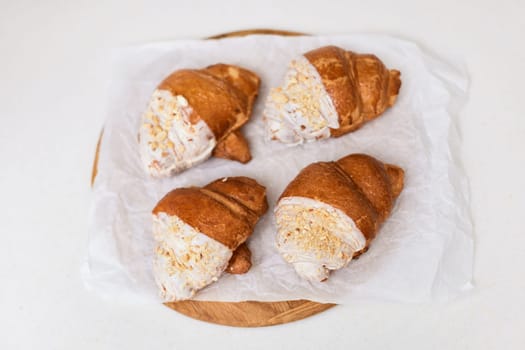 fresh croissants on wooden tray on white table, top view