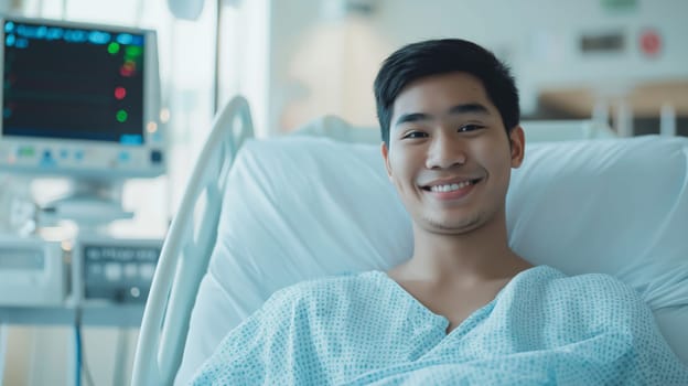 A young southeast asian man in his mid20s lies in a hospital bed, smiling at the camera. he is dressed in a hospital gown, and there is a medical monitor in the background. the setting reflects a calm and supportive healthcare environment, emphasizing recovery and wellbeing.