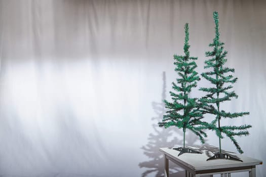 A Christmas tree stands on a table, casting a shadow against a plain backdrop in a cozy indoor setting