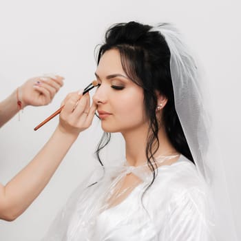 make-up artist hands with a brush makes up and apply shadows on the eyes of the bride's girl in the beauty salon