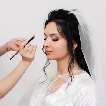 make-up artist hands with a brush makes up and apply shadows on the eyes of the bride's girl in the beauty salon