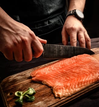 Chief cooking salmon for dinner, cutting red fish on a cutting board in the kitchen
