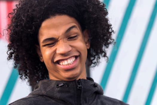 close up portrait of a funny black male teenager with curly hair laughing happy looking at camera, concept of happiness and young lifestyle
