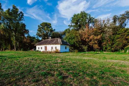 Traditional rural house with a thatched roof is nestled in a peaceful countryside surrounded by trees and greenery.