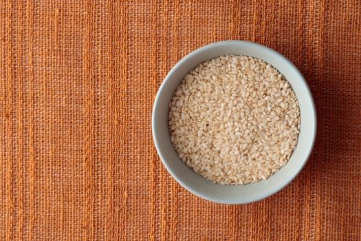 Close-up of Organic White Sesame seeds, Sesamum indicum in a ceramic bowl with brown background, ingredient o kimchi. Top view