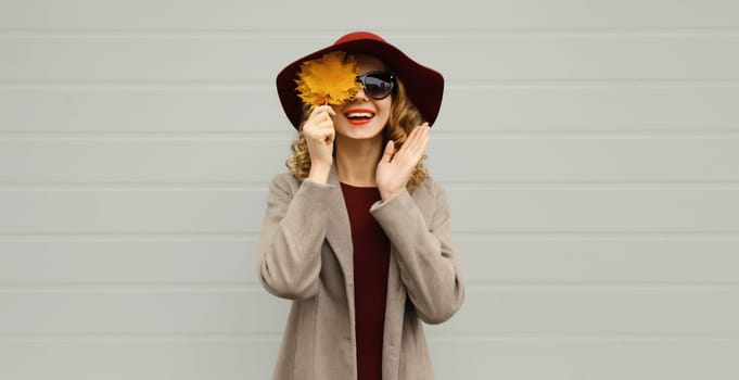 Autumn portrait of beautiful surprised happy smiling woman with yellow maple leaves, stylish joyful girl posing on gray background